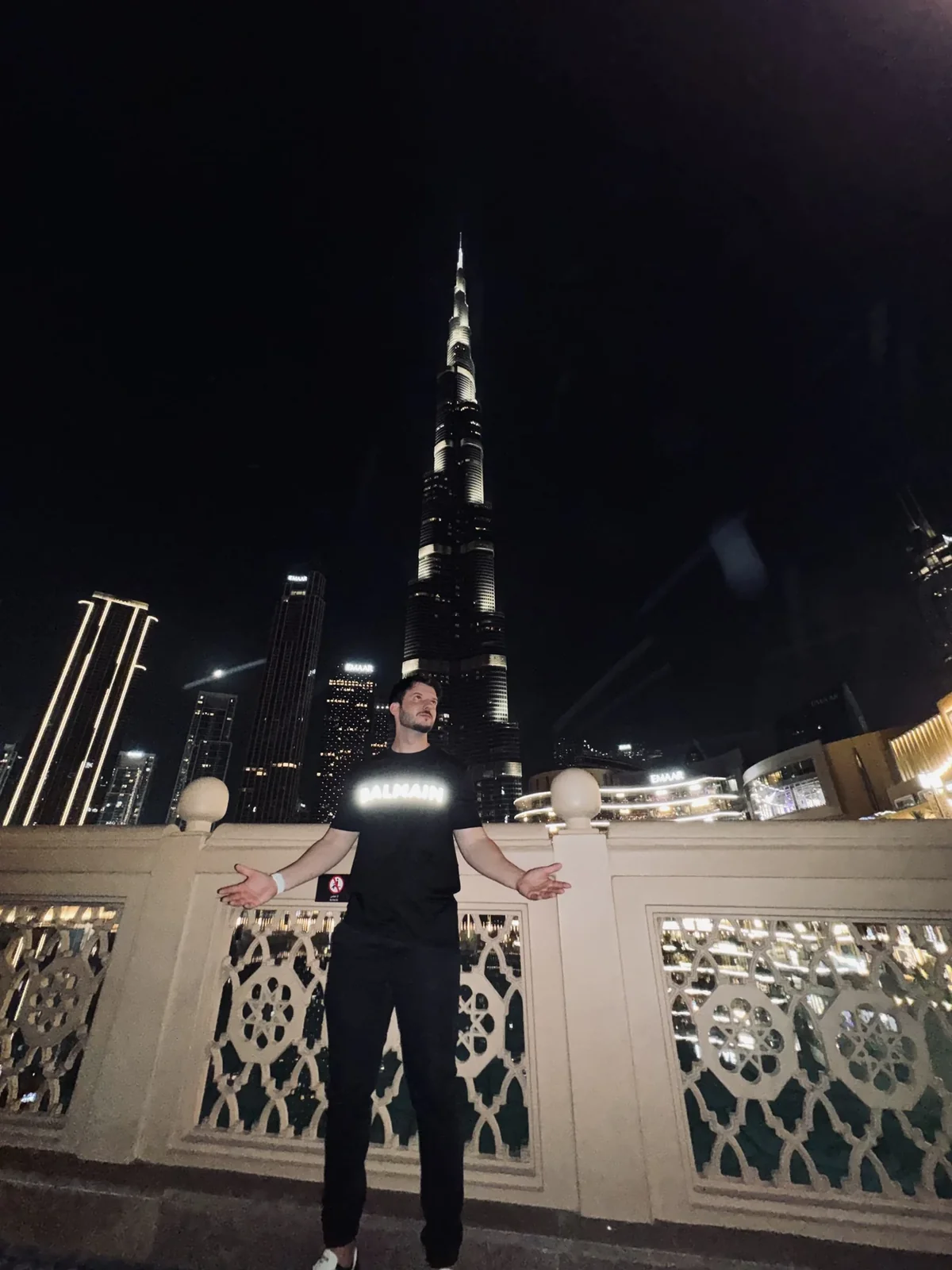 Bruno Emigdio de braços abertos diante do Burj Khalifa à noite